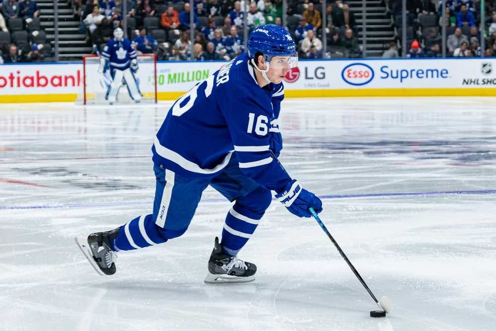 Mitchell Marner wearing his blue and white home Maple Leafs' jersey is skating across the ice with the puck on his stick.